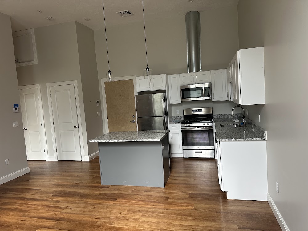 Kitchen with white cabinets, granite island, and warm wood-look flooring